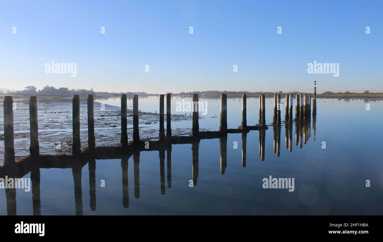 Mooring posts at Bosham Quay reflected in the water. Stock Photo