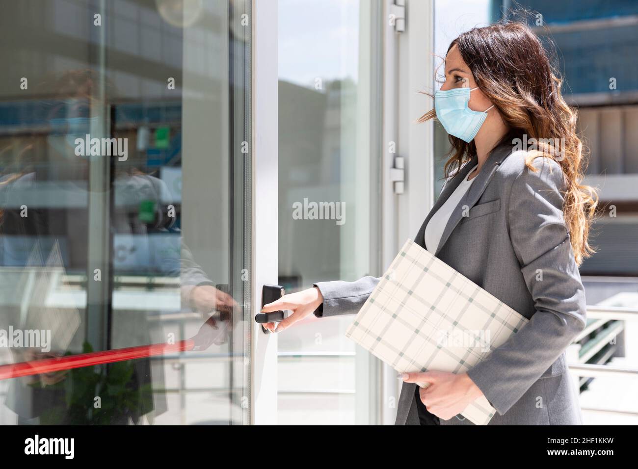 Elegant young Caucasian businesswoman entering her workplace. She is wearing a medical mask to prevent the spread of the Covid-19 virus. Space for tex Stock Photo