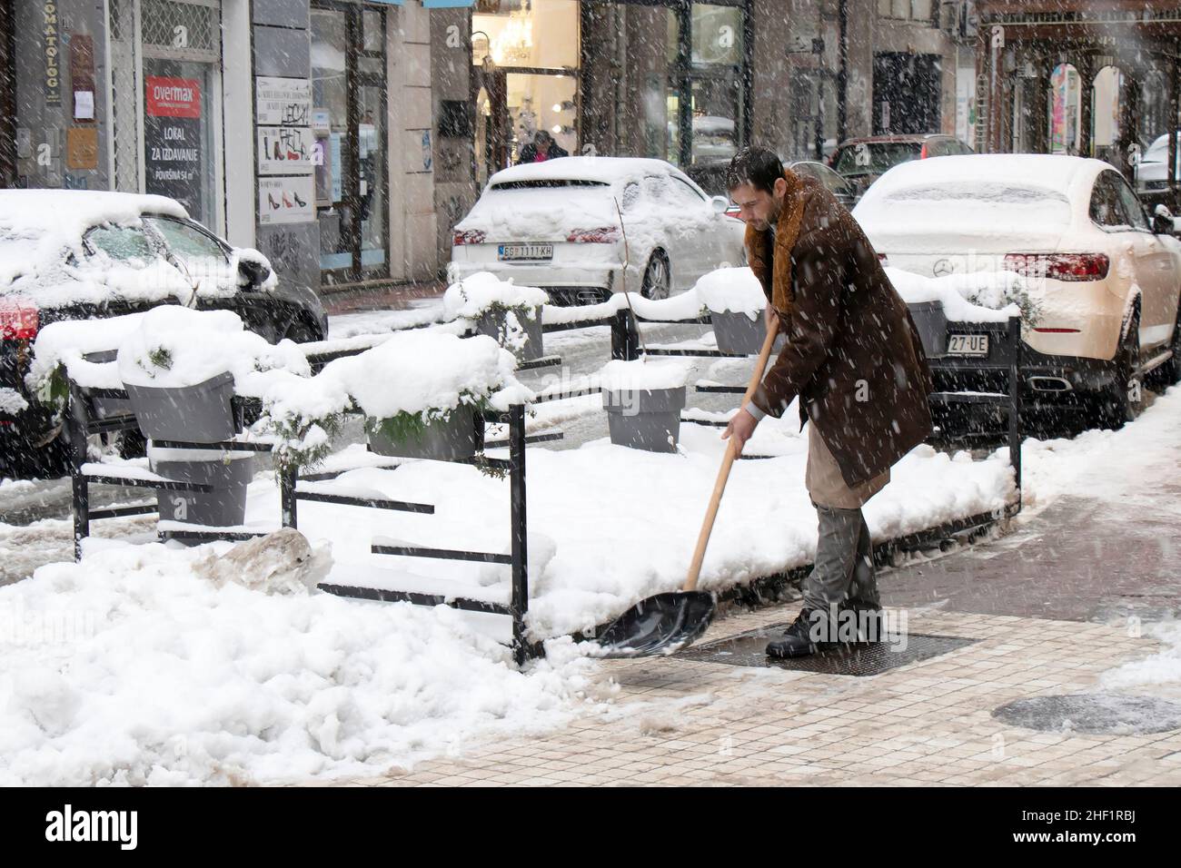 Belgrade, Serbia - January 11, 2022: One man using shovel for removing snow from city sidewalk in front of the coffee bar Stock Photo