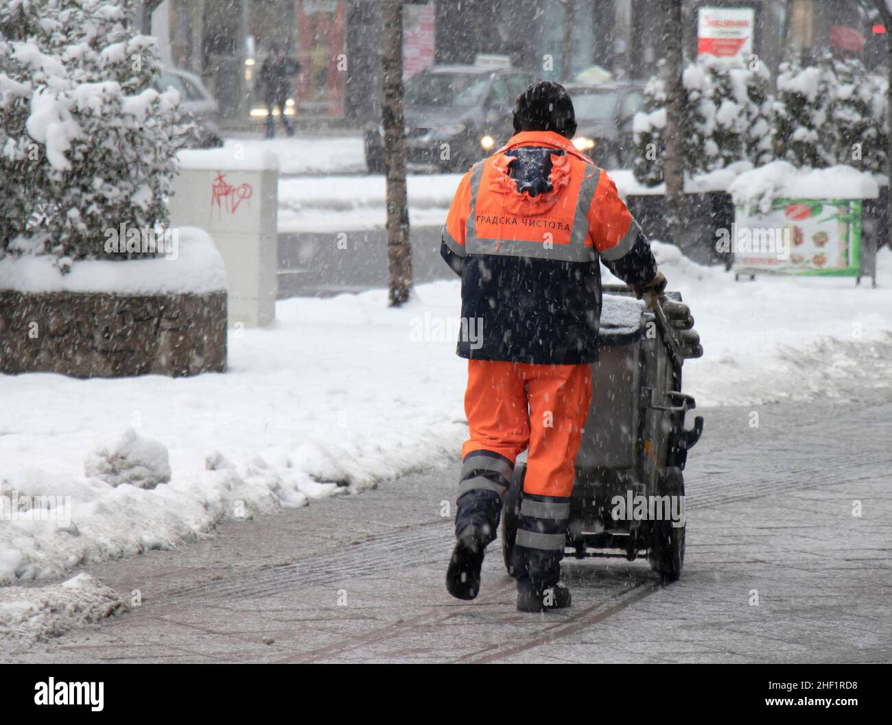 Belgrade, Serbia - January 11, 2022: One man working for city cleaning service pushing the collector bin on city street as walking away, on a snowy wi Stock Photo