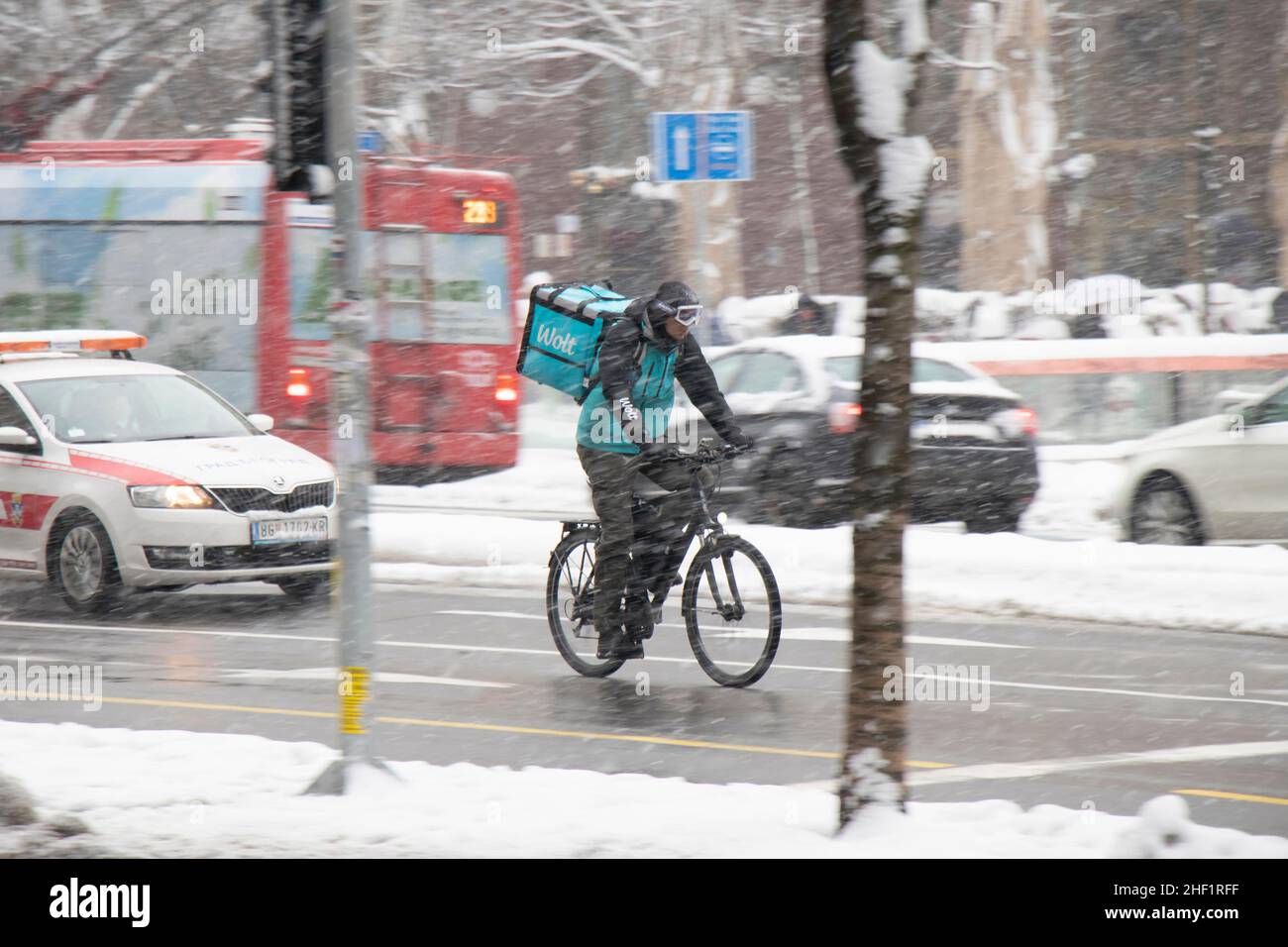 Belgrade, Serbia - January 11, 2022: Winter city traffic in heavy snow storm, and one Wolt delivery courier riding a bicycle on city street Stock Photo