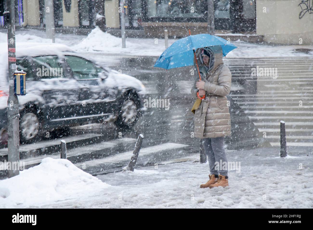 Belgrade, Serbia - January 11, 2022: Woman waiting at crossroad under blue umbrella on a snowy city street during heavy snow fall Stock Photo