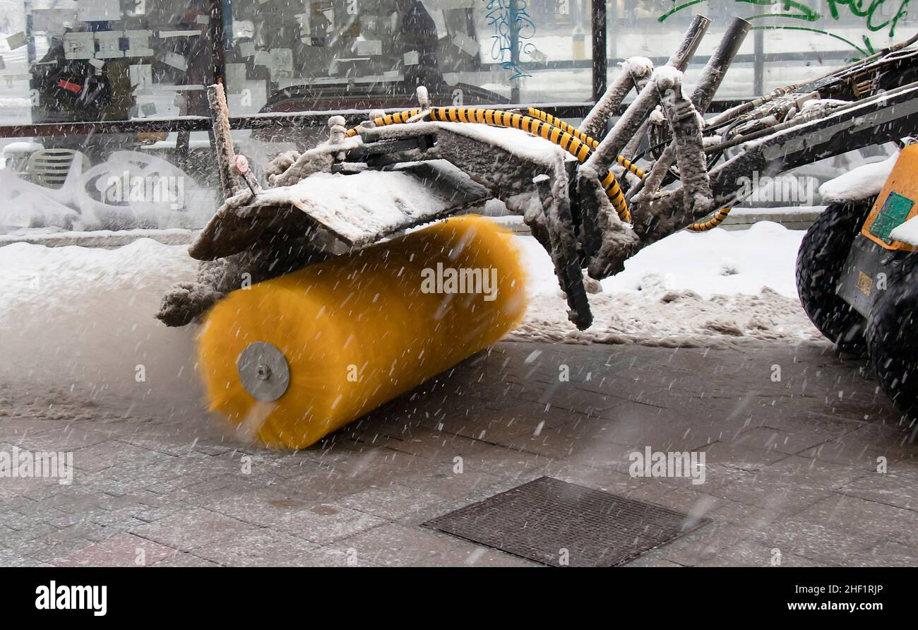 Snow removal machine with broom clearing snow dusting from sidewalk walkway in winter maintenance city service routine, detail Stock Photo