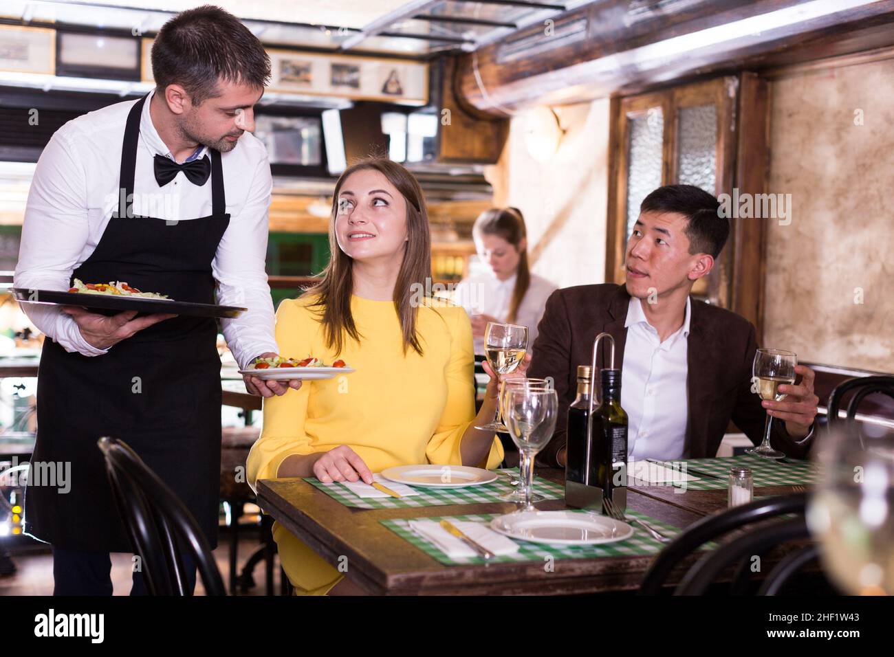 Man waiter is brings order to couple who have dinner and drink wine Stock Photo