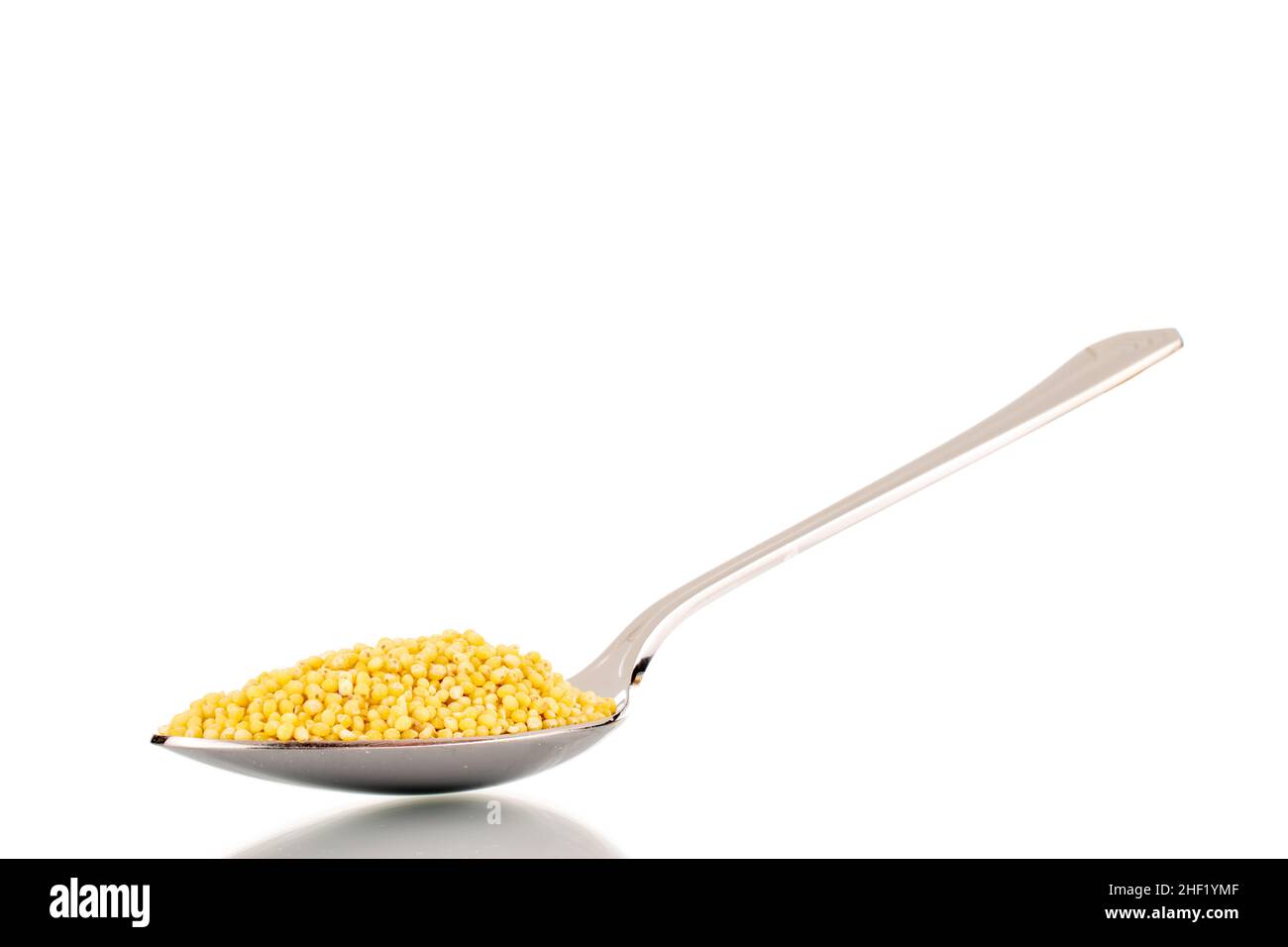 Uncooked organic millet groats with metal spoon, closeup, isolated on