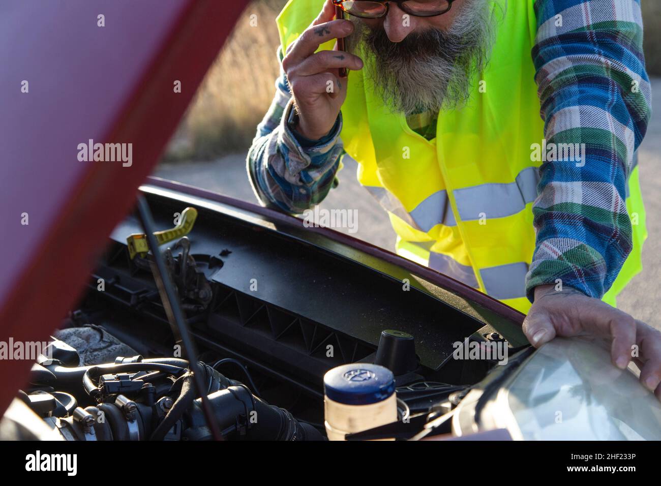 Hispanic talking on the phone to ask a mechanic to come fix his broken down car on the road Stock Photo