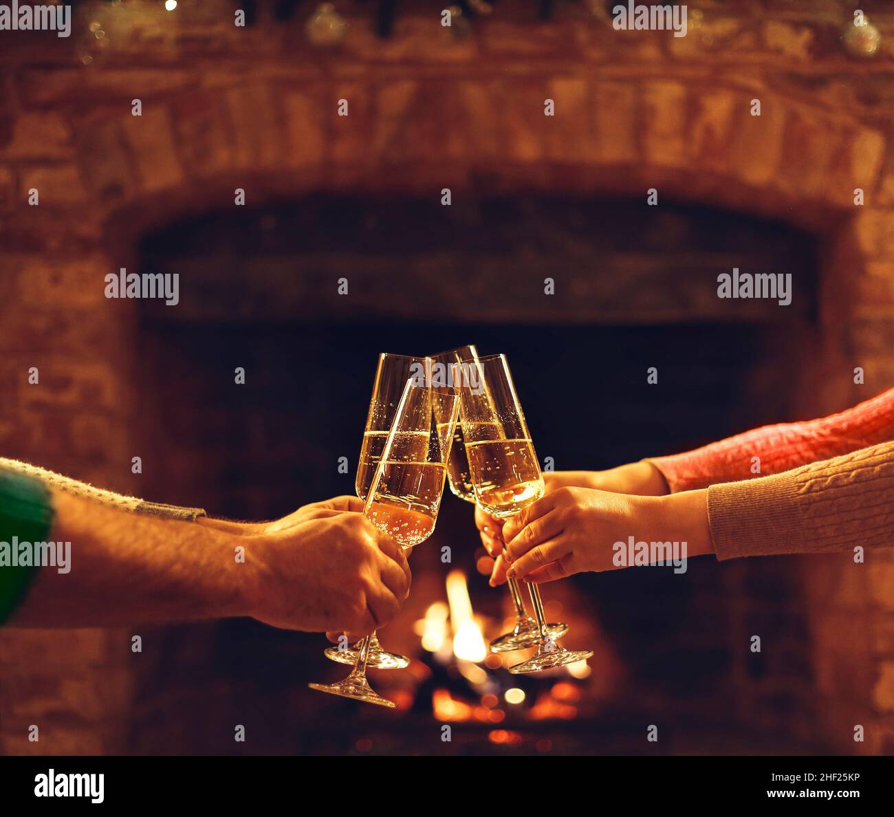 People Clinking Champagne Glasses While Gathering Around Fireplace In Country House Cropped