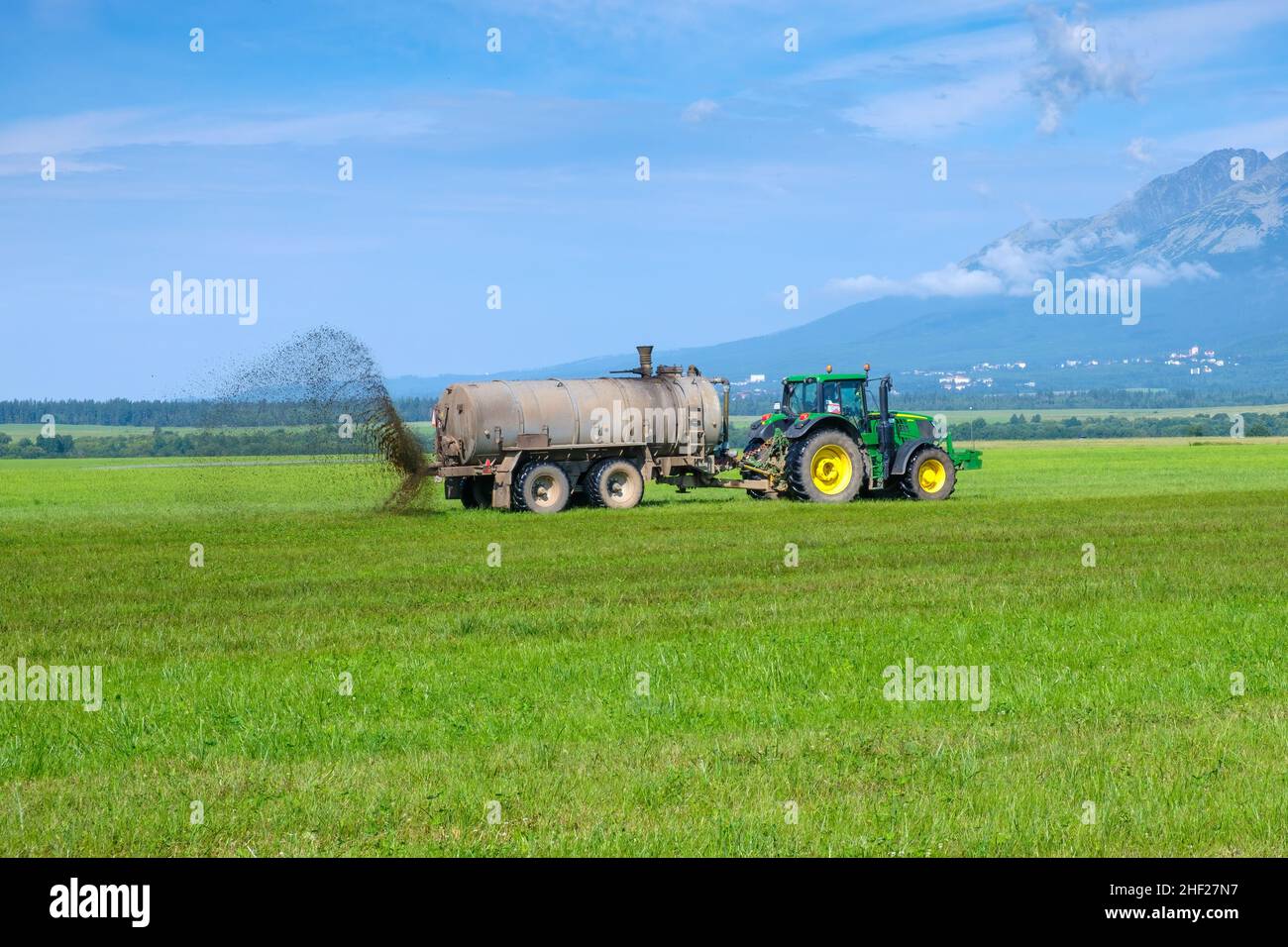 A big tractor spreading fertilizer to improve the harvest on pasture meadow or field in the High Tatra mountains. Landfarming concept. January 2022, Poprad, Slovakia.  Stock Photo