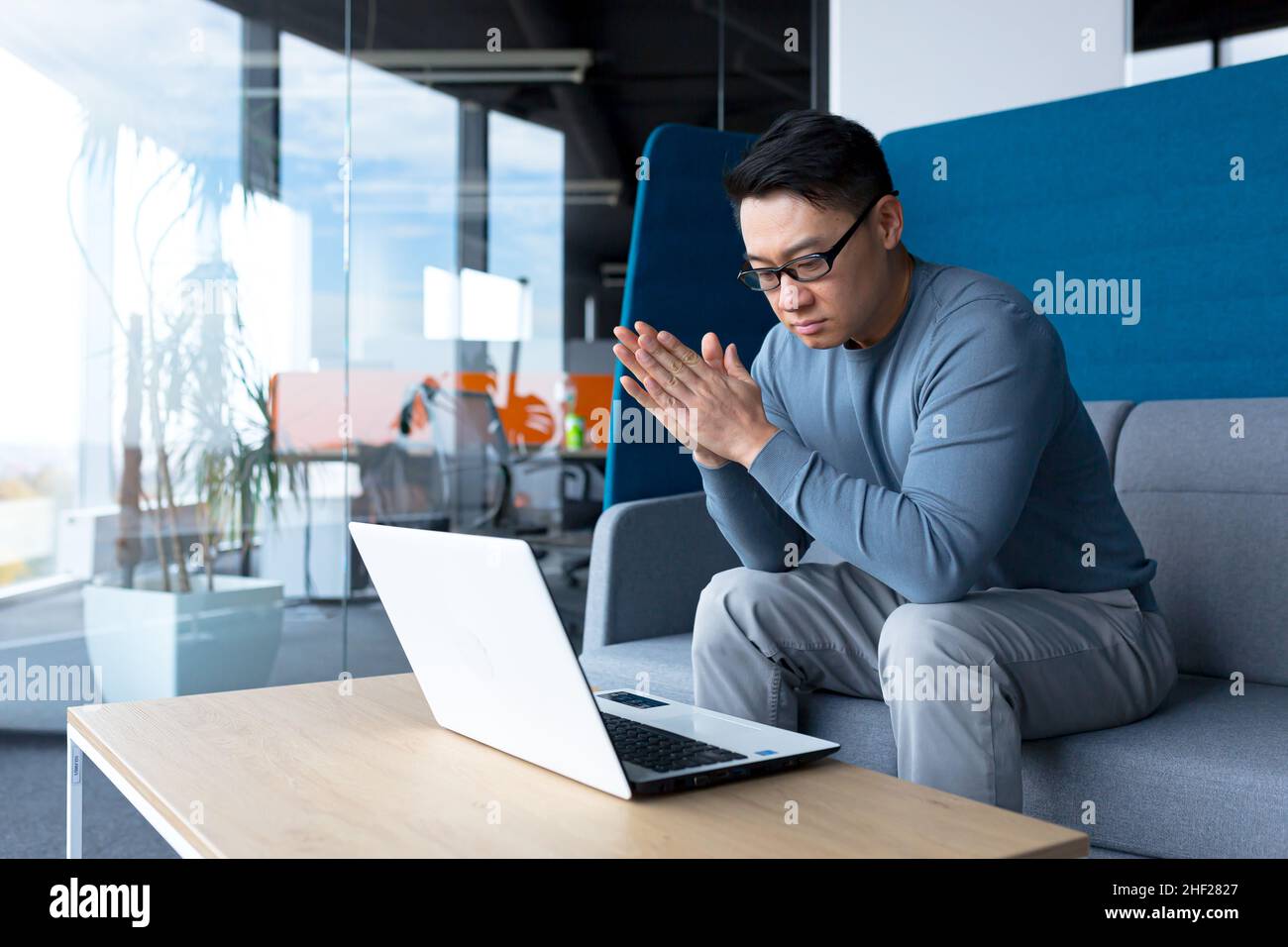 Pensive asian man working from office sitting at desk, making important