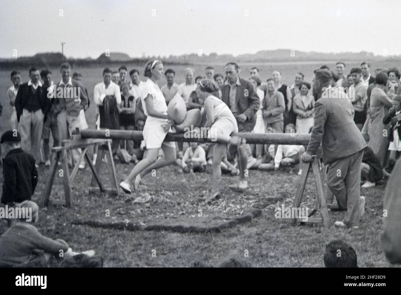 Vintage Image or Black and White Photosgraph or Spectators and Players in a Traditional Pilow Fight Game on Wooden Beam Played in an English Holiday Camp in the 1930s England Stock Photo