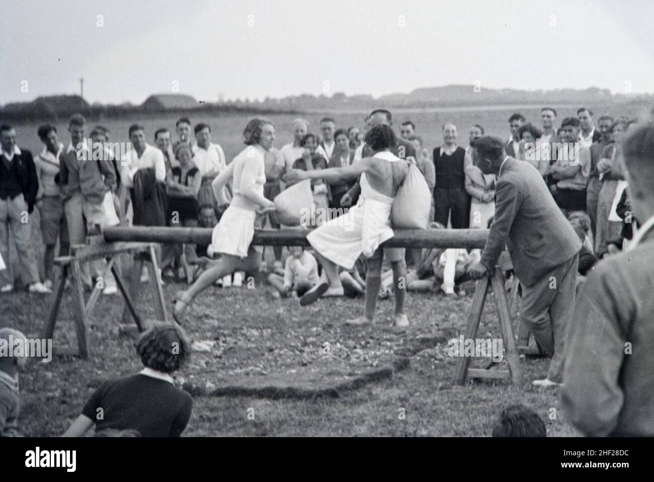 Vintage Image or Black and White Photograph of Spectators and Players in a Traditional Pillow Fight Game on Wooden Beam Played in an English Holiday Camp in the 1930s England Stock Photo