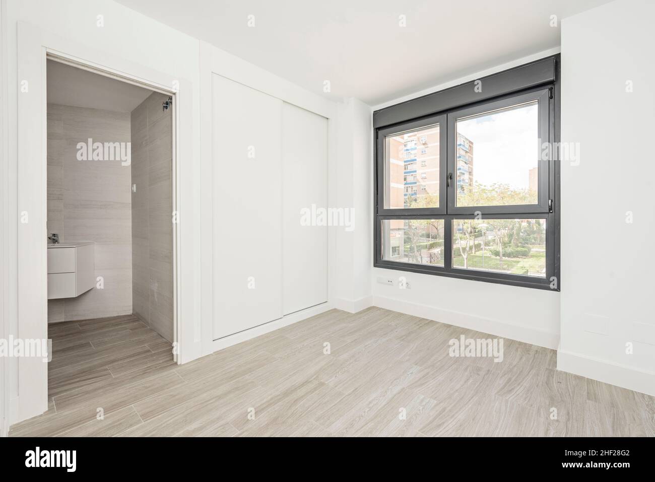 Room with built-in wardrobe with white sliding doors, en suite bathroom and large black aluminum window Stock Photo