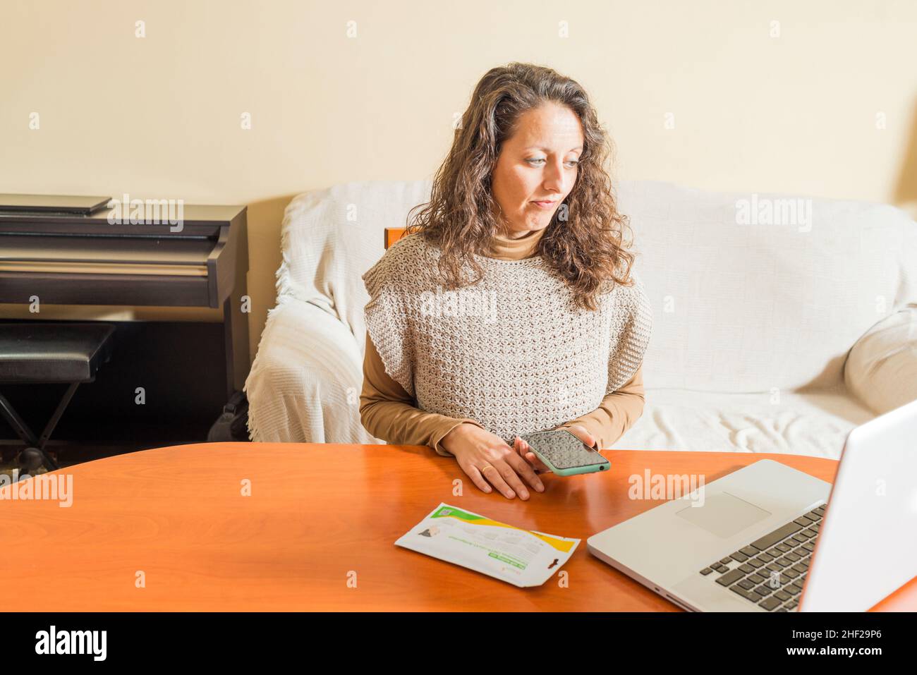 A woman with a smartphone and in front of a laptop looking up information about Covid19 antigen self-tests on the internet. Stock Photo