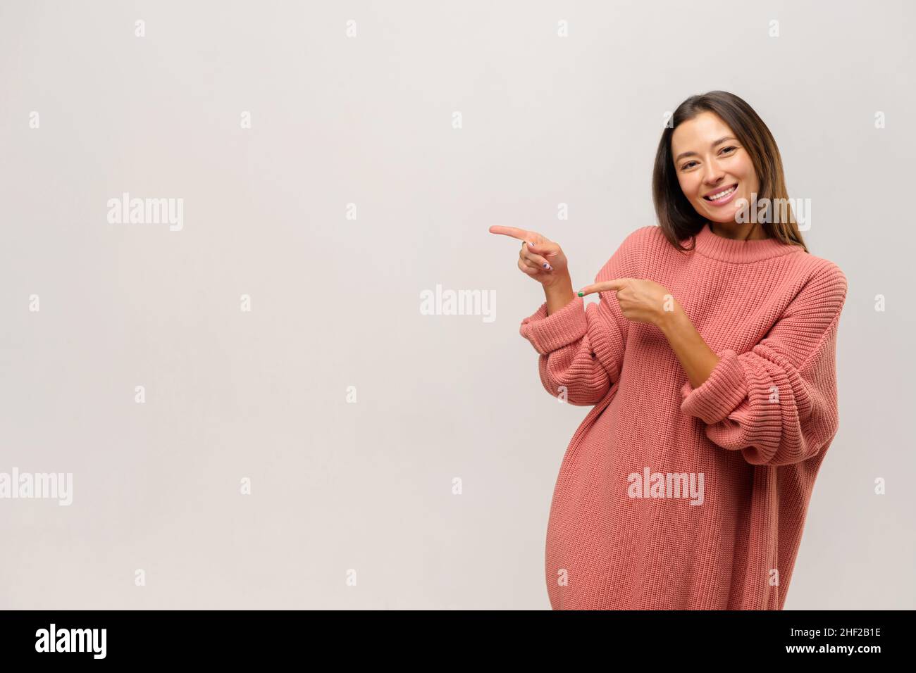 Asian woman pointing aside with fingers, having happy facial expression. Indoor studio shot isolated on white background Stock Photo