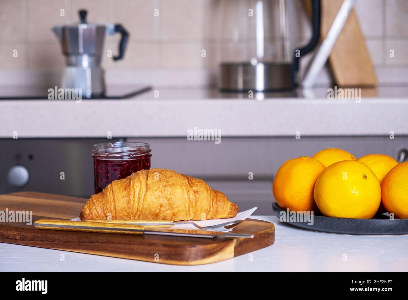 Fresh croissant and jam and dish of oranges lies on kitchen table Stock Photo