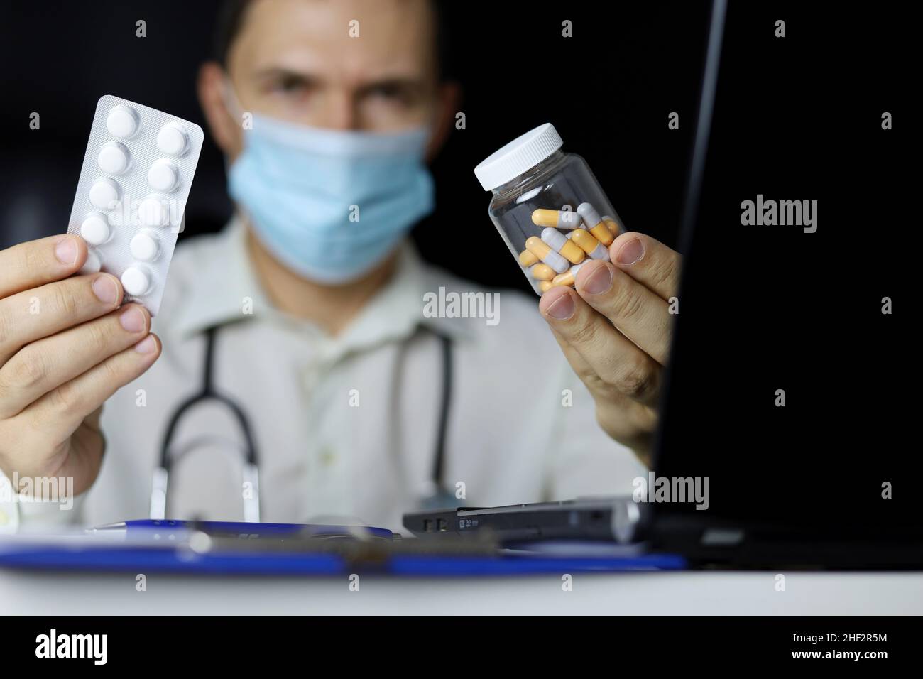 Pills and capsules in hand of doctor in medical mask sitting at laptop in office. Concept of prescription, choice of medicines, antibiotics or vitamin Stock Photo