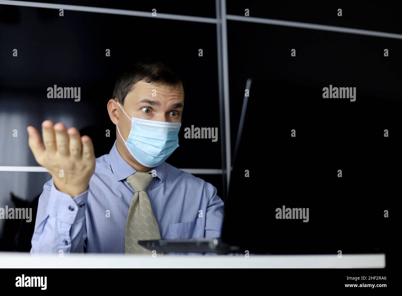 Shocked man in face mask looking at laptop display. Office worker disappointed or surprised by an unexpected error on computer device Stock Photo
