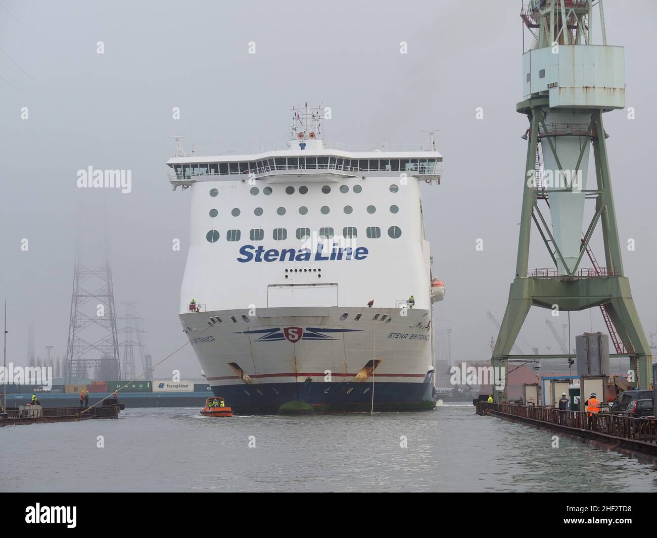 Stena Line ferry Stena Brittanica being manoeuvred into a dry dock in the port of Antwerp, Belgium. The small boat brings the cables to shore to attac Stock Photo