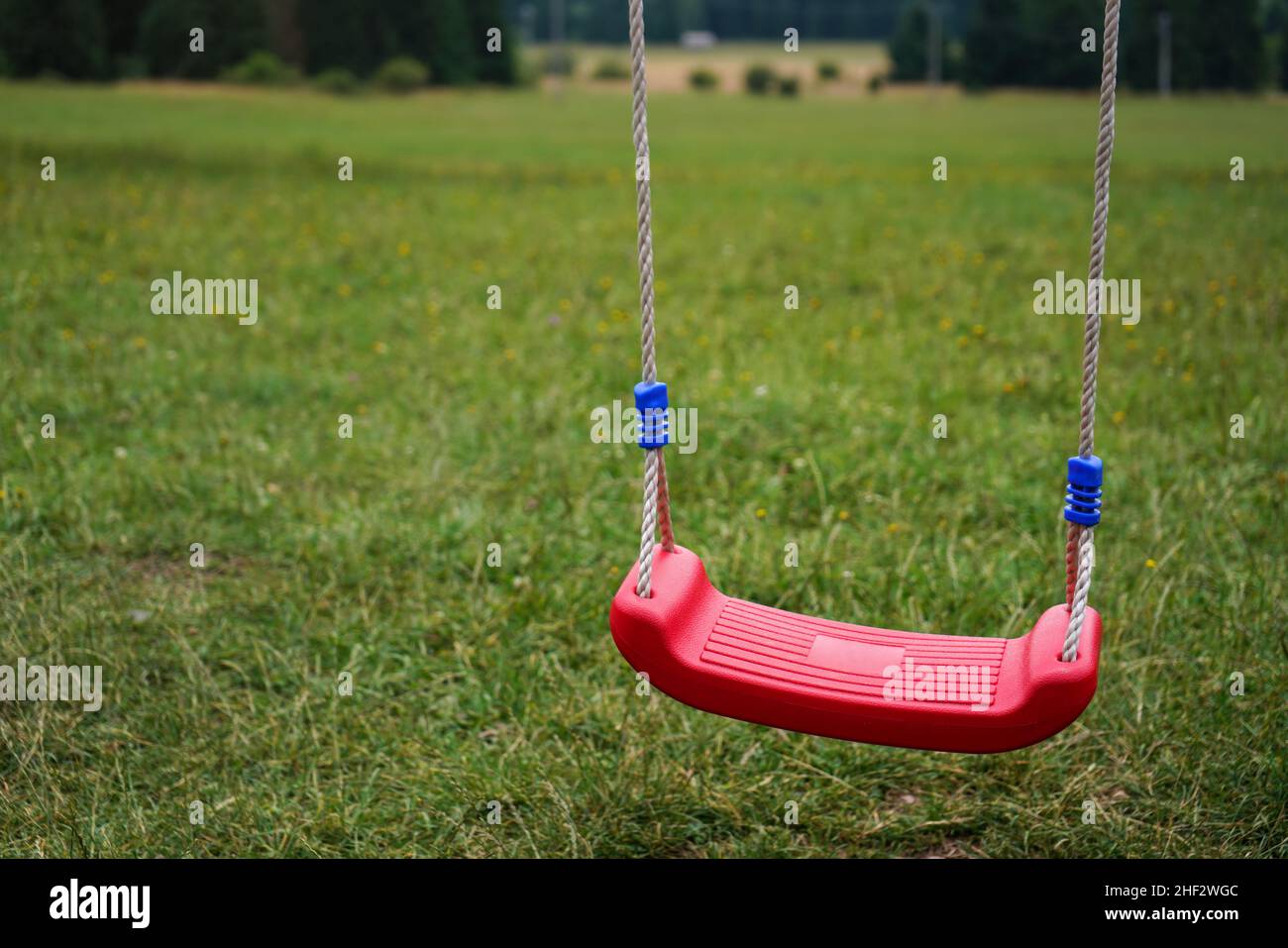 Small plastic kid hanging swing, blurred meadow in background Stock Photo