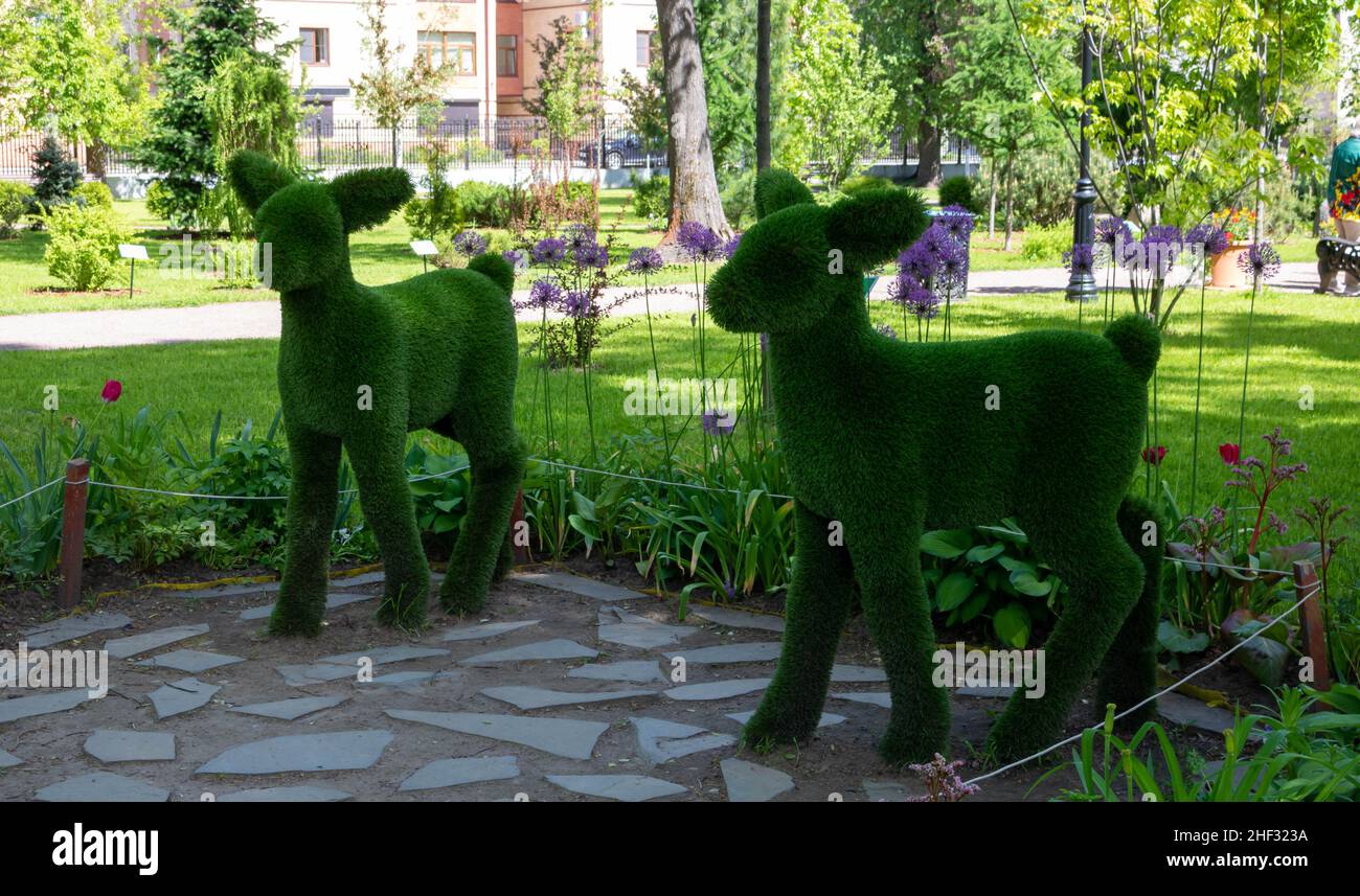 Sculptures of two fawns in a green park against a background of trees and flowers on a bright sunny day. Stock Photo