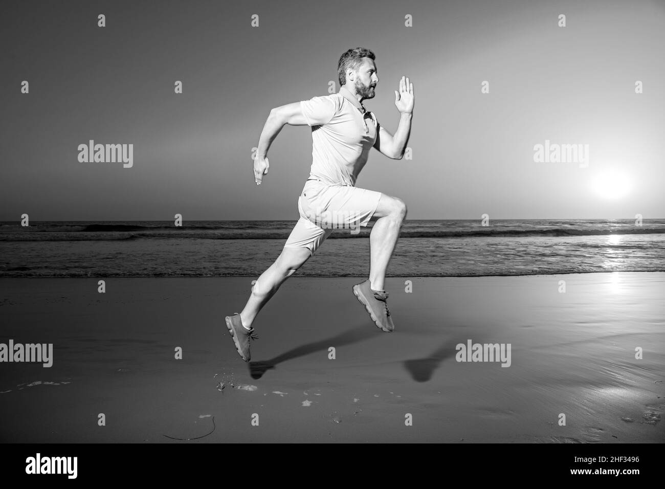 Man running at sunset. Full length of healthy man running and sprinting outdoors. Male runner. Fit man fitness model working outdoor by sea beach. Run Stock Photo