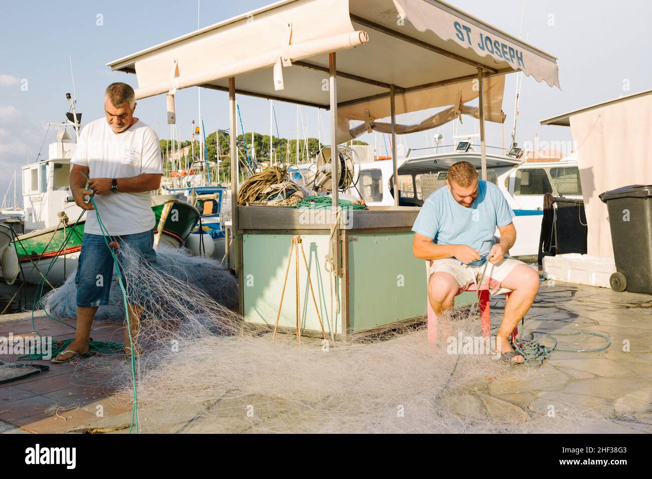 Two fisherman who are twin brothers mending their nets after a fishing trip at first light in the small French fishing port of Sanary sur Mer, Cote d' Azur in the south of France. 2014. Stock Photo