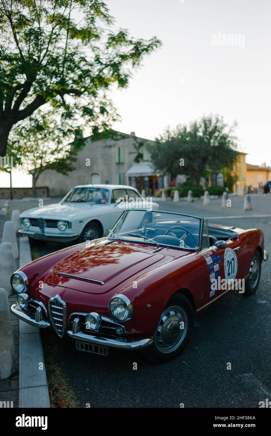 A red Alfa Romeo Giulia Spider 1600 Veloce and a white 1600 Giulia Sprint GT Veloce parked in the picturesque French hilltop village of Le Castellet. Stock Photo