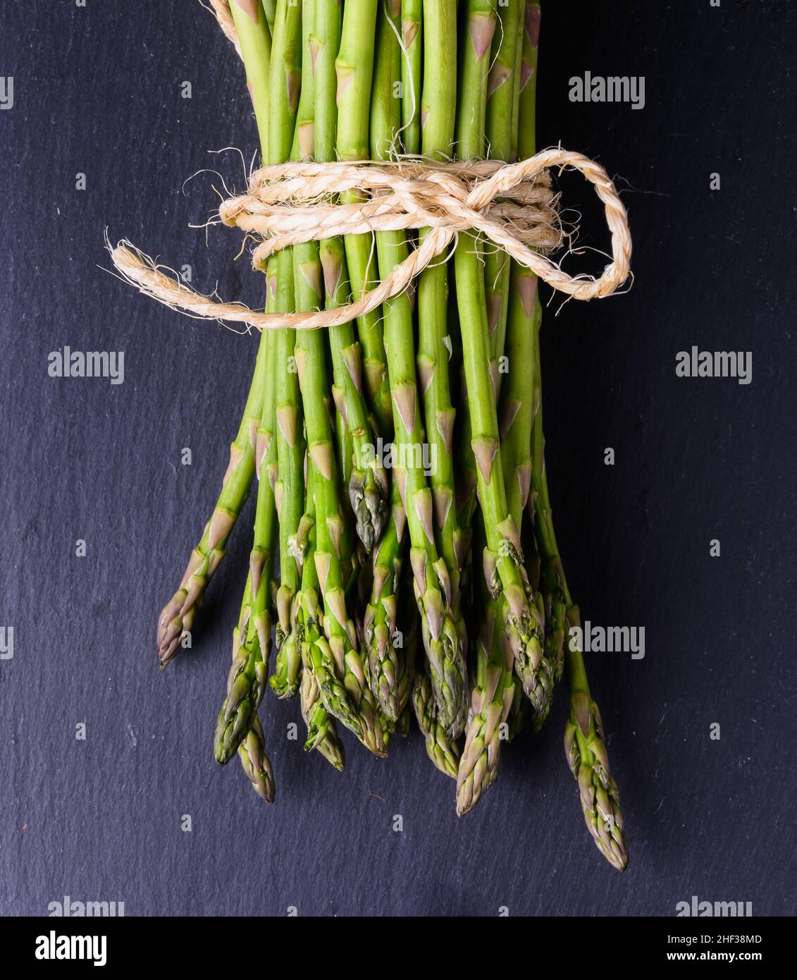 Fresh green asparagus tied with a string on a slate and rustic wooden table  Stock Photo