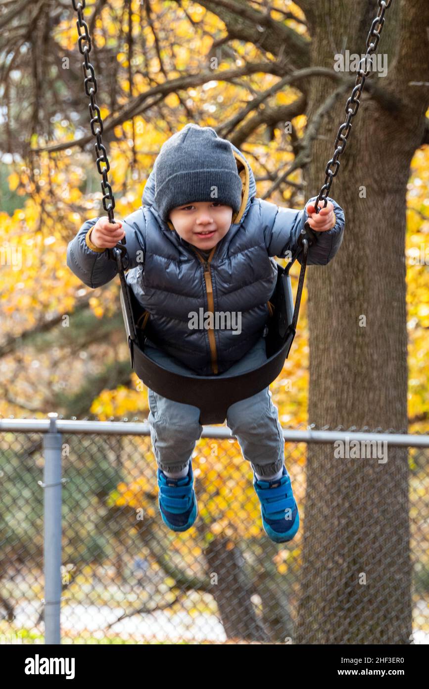 Two year old boy swinging on city park swing set; Corinthian Gardens; Philadelphia; Pennsylvania; USA Stock Photo