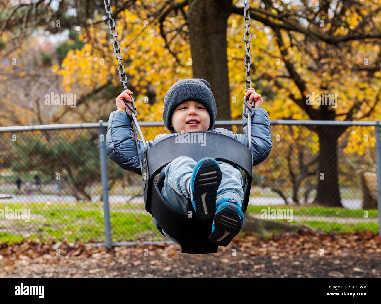 Two year old boy swinging on city park swing set; Corinthian Gardens; Philadelphia; Pennsylvania; USA Stock Photo