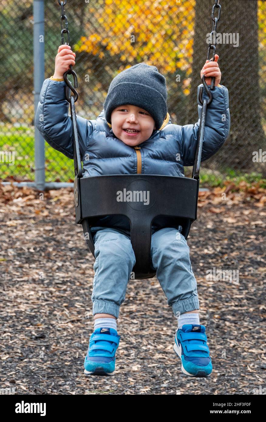 Two year old boy swinging on city park swing set; Corinthian Gardens; Philadelphia; Pennsylvania; USA Stock Photo