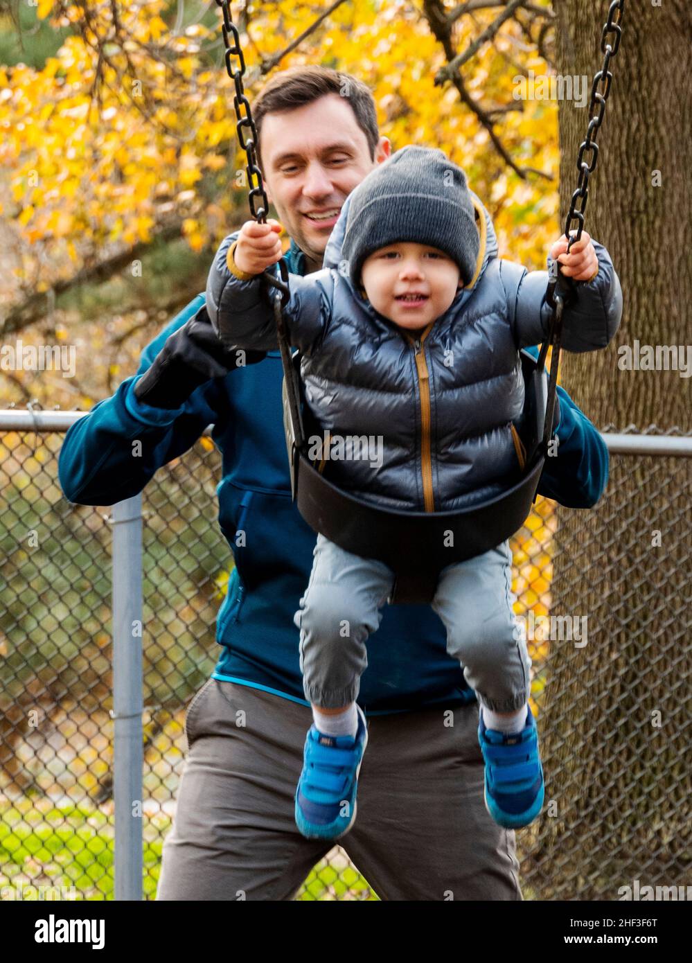 Father pushing two year old boy swinging on city park swing set; Corinthian Gardens; Philadelphia; Pennsylvania; USA Stock Photo