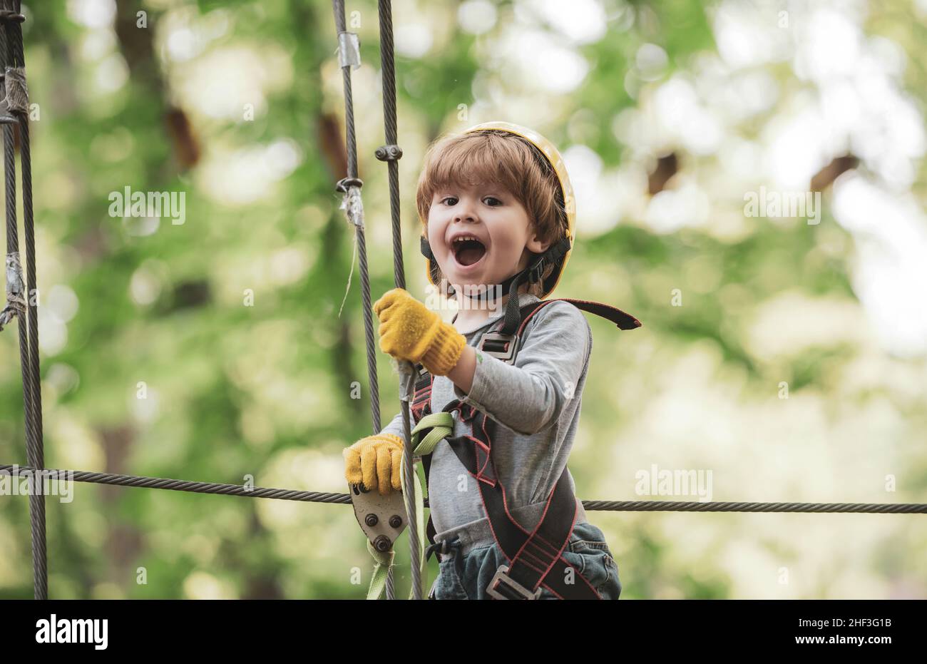Cargo net climbing and hanging log. Portrait of a beautiful kid on a rope park among trees. Rope park - climbing center. Safe Climbing extreme sport Stock Photo