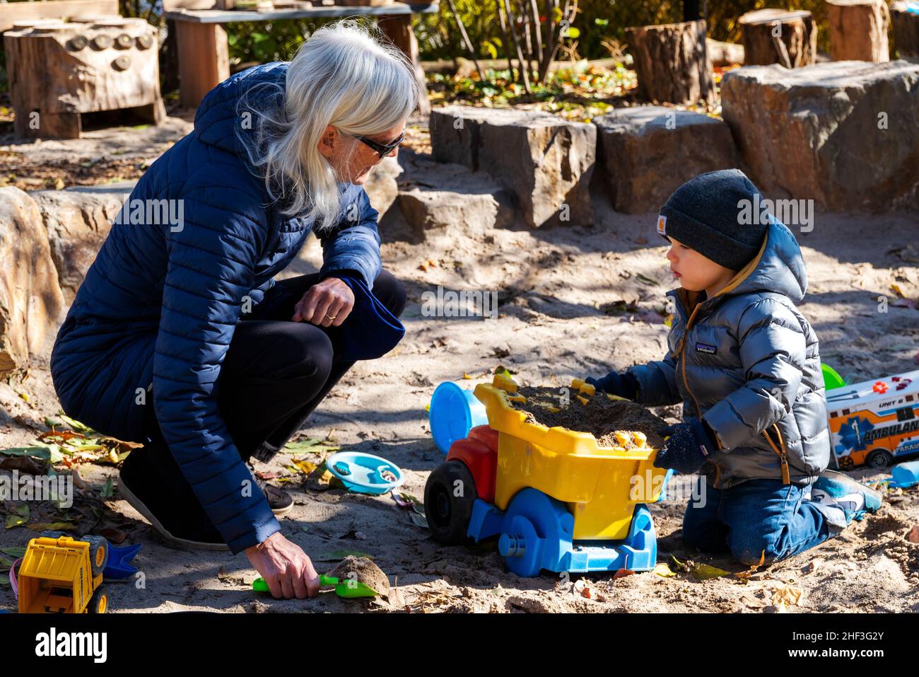 Senior aunt playing in park sandbox with two year old nephew Stock Photo