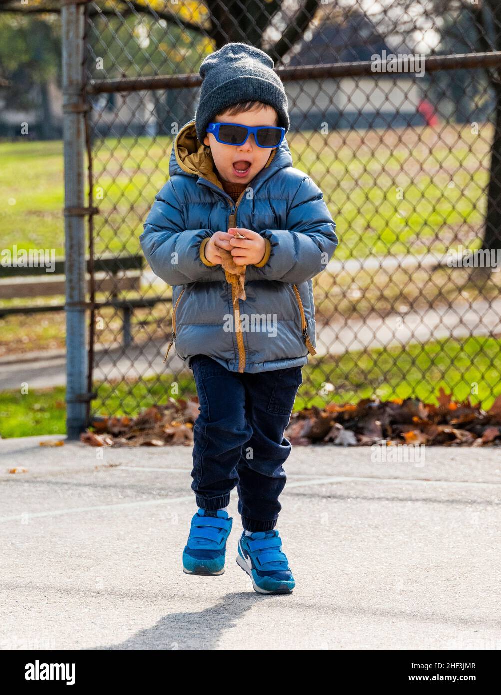 Two year old boy with sunglasses running on city park playground; Corinthian Gardens; Philadelphia; Pennsylvania; USA Stock Photo
