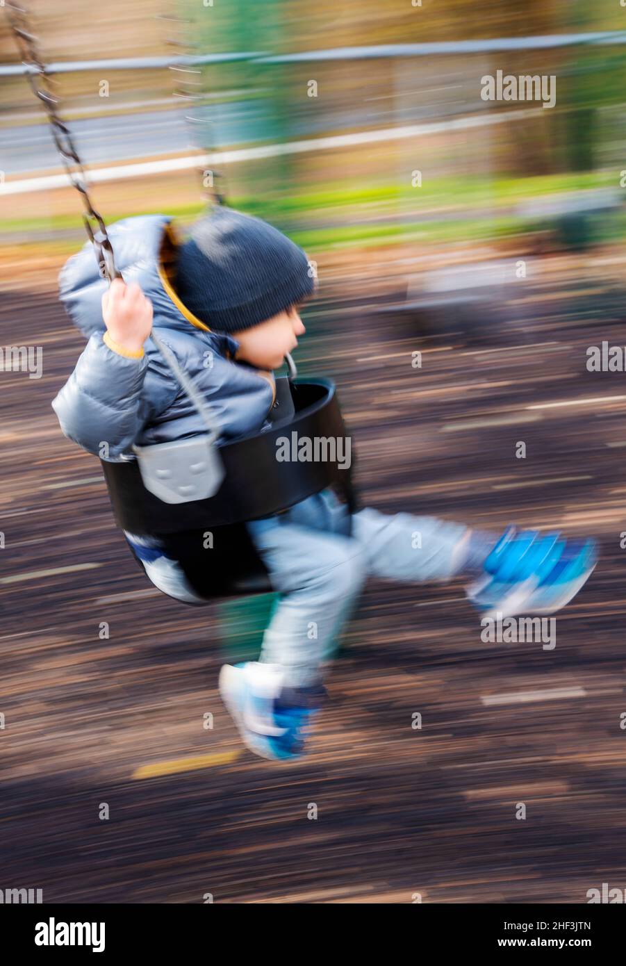 Blur - pan - action photo of two year old boy swinging on city park swing set; Corinthian Gardens; Philadelphia; Pennsylvania; USA Stock Photo