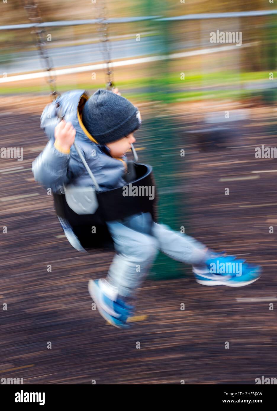 Blur - pan - action photo of two year old boy swinging on city park swing set; Corinthian Gardens; Philadelphia; Pennsylvania; USA Stock Photo