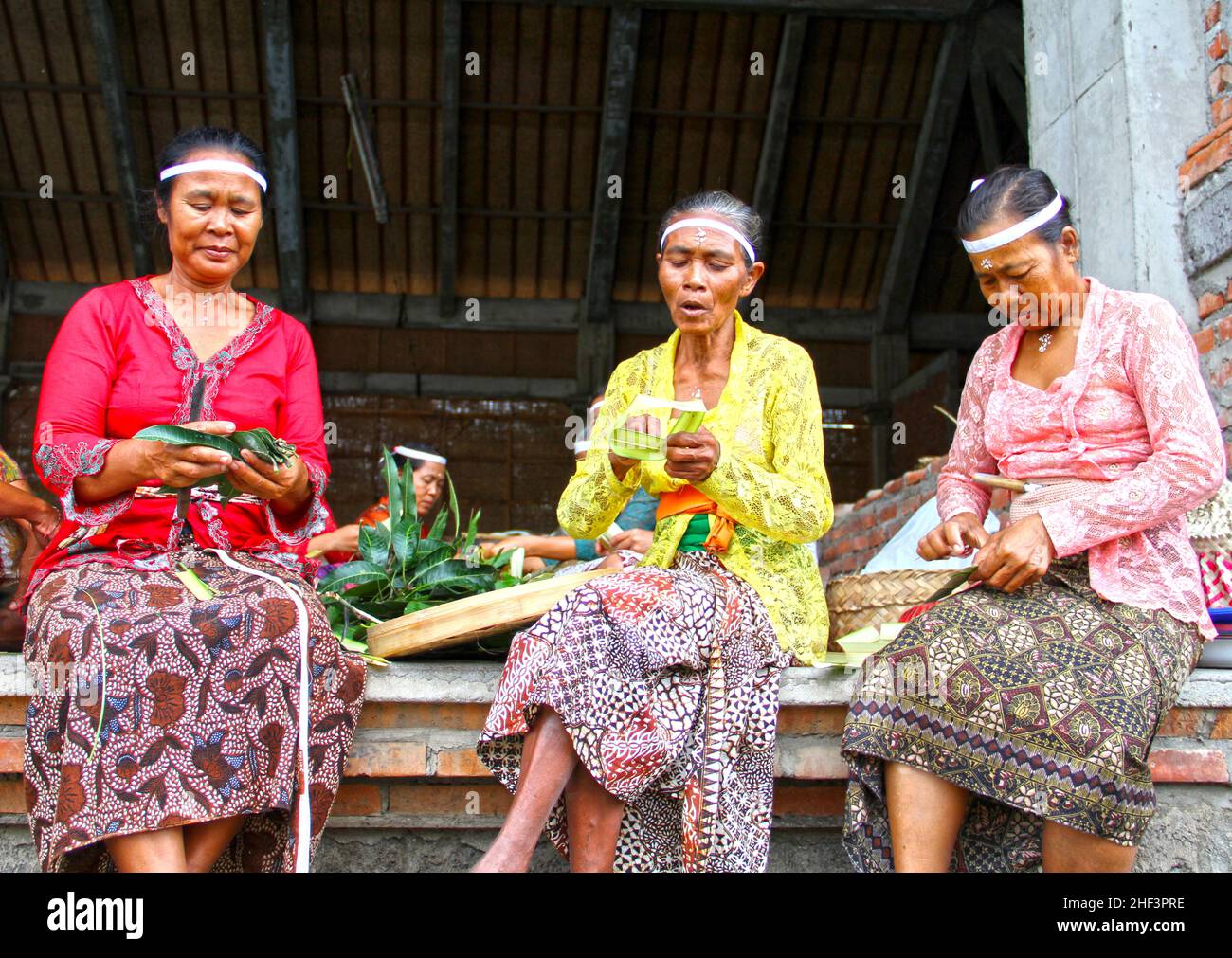 Colorfully traditionally dressed women makling Canang Sari Hindu offerings for a ceremony taking place in the village of Ketewel in Gianyar, Stock Photo