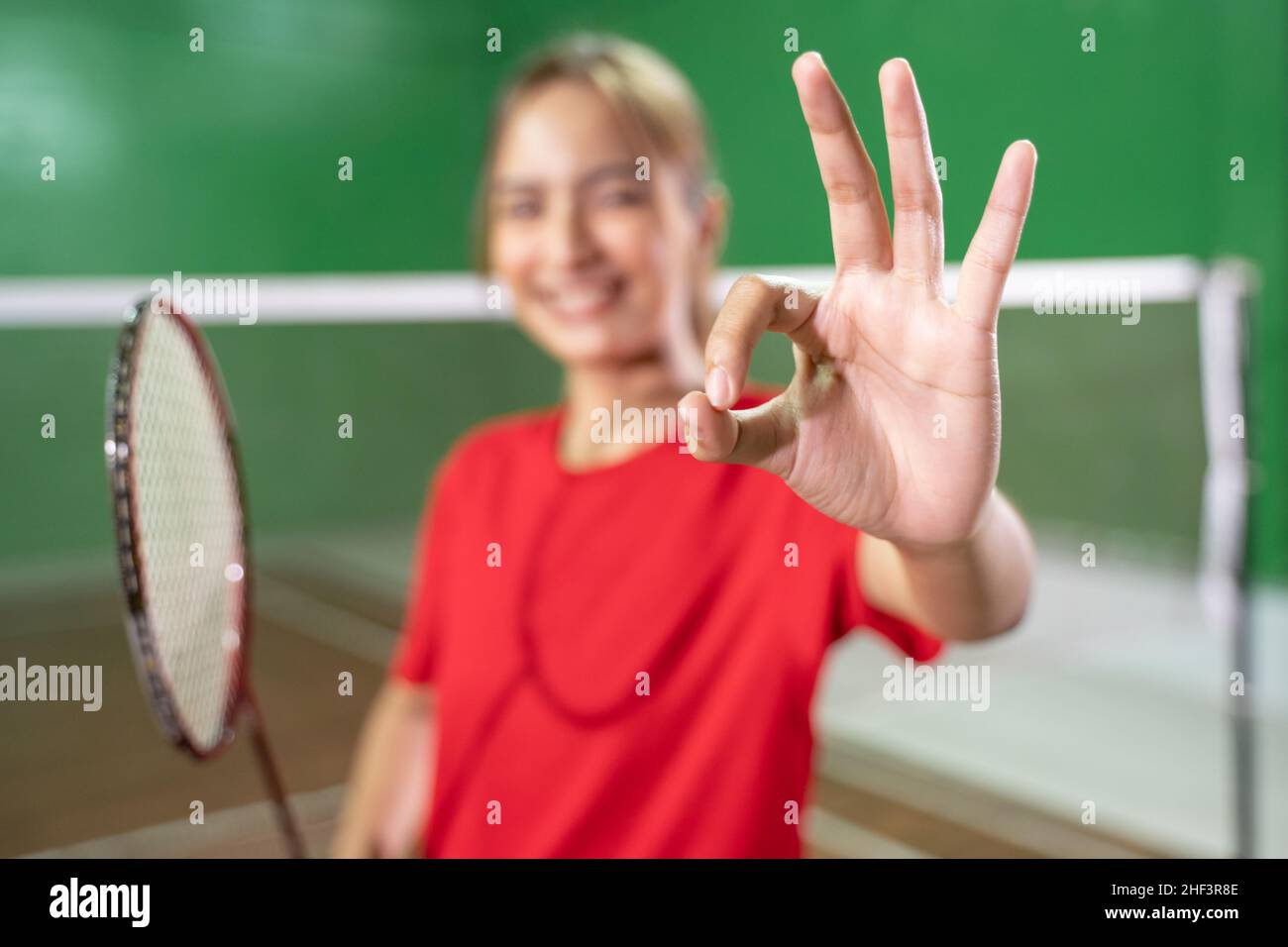 Asian girl badminton player with okay hand gesture holding racket Stock