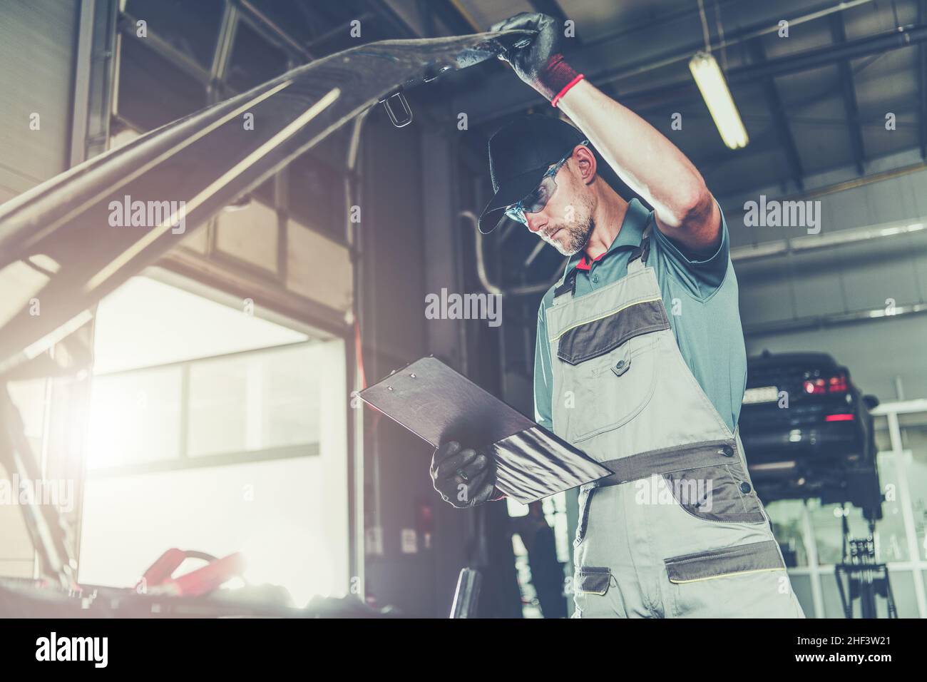 Caucasian Car Mechanic Electronic Elements Technician Checking on an Issue with a Vehicle Looking Under Its Hood. Automotive Service Industry. Stock Photo