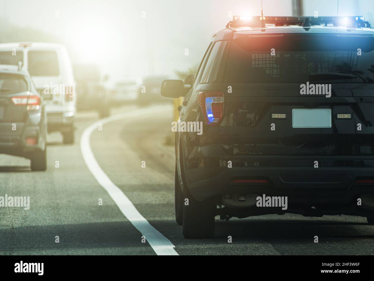 Flashing Lights of American Modern Highway Police Patrol Cruiser on Side of a Road. Rear View. Transportation and Police Enforcement Theme. Stock Photo