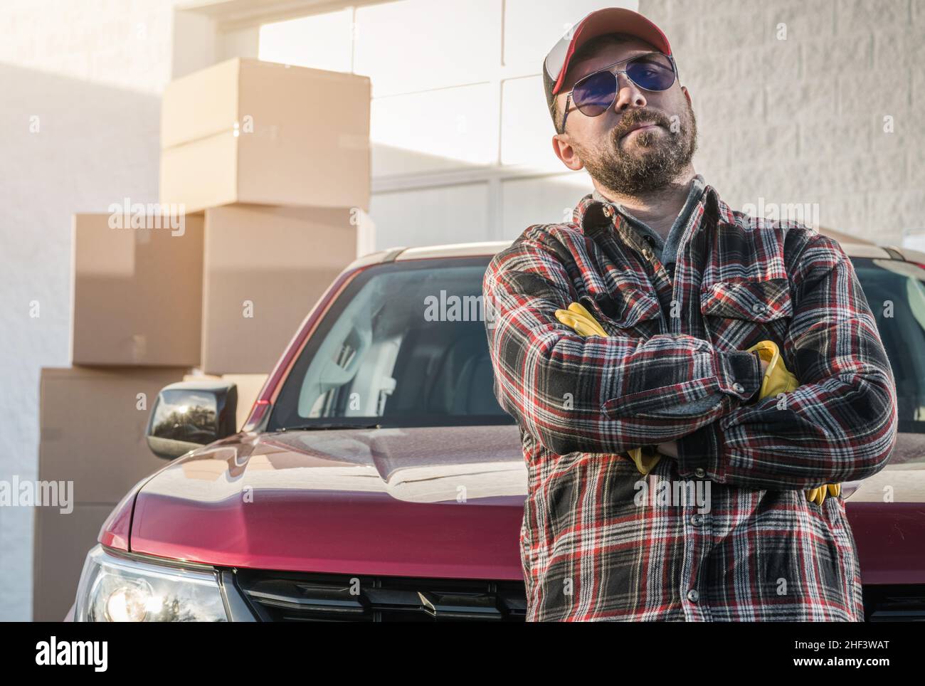Proud Caucasian Contractor Worker in His 30s Wearing Sunglasses Next to His Modern Pickup Truck and Cargo Boxes. Supplies Delivery Theme. Stock Photo