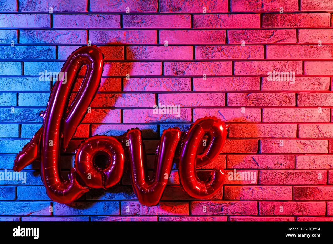 Balloon in shape of word LOVE hanging on color brick wall. Valentine's Day celebration Stock