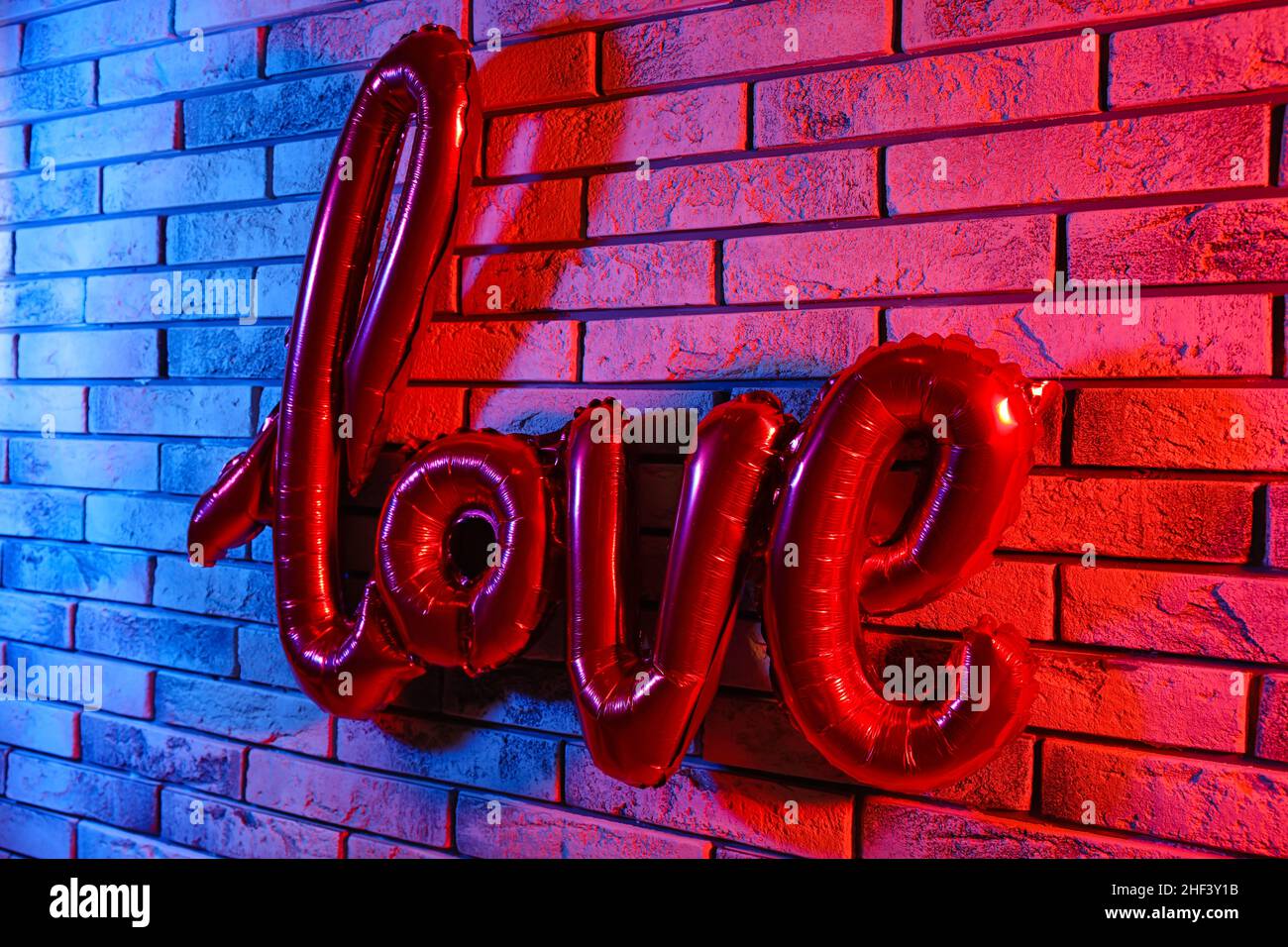 Balloon in shape of word LOVE hanging on color brick wall. Valentine's Day celebration Stock