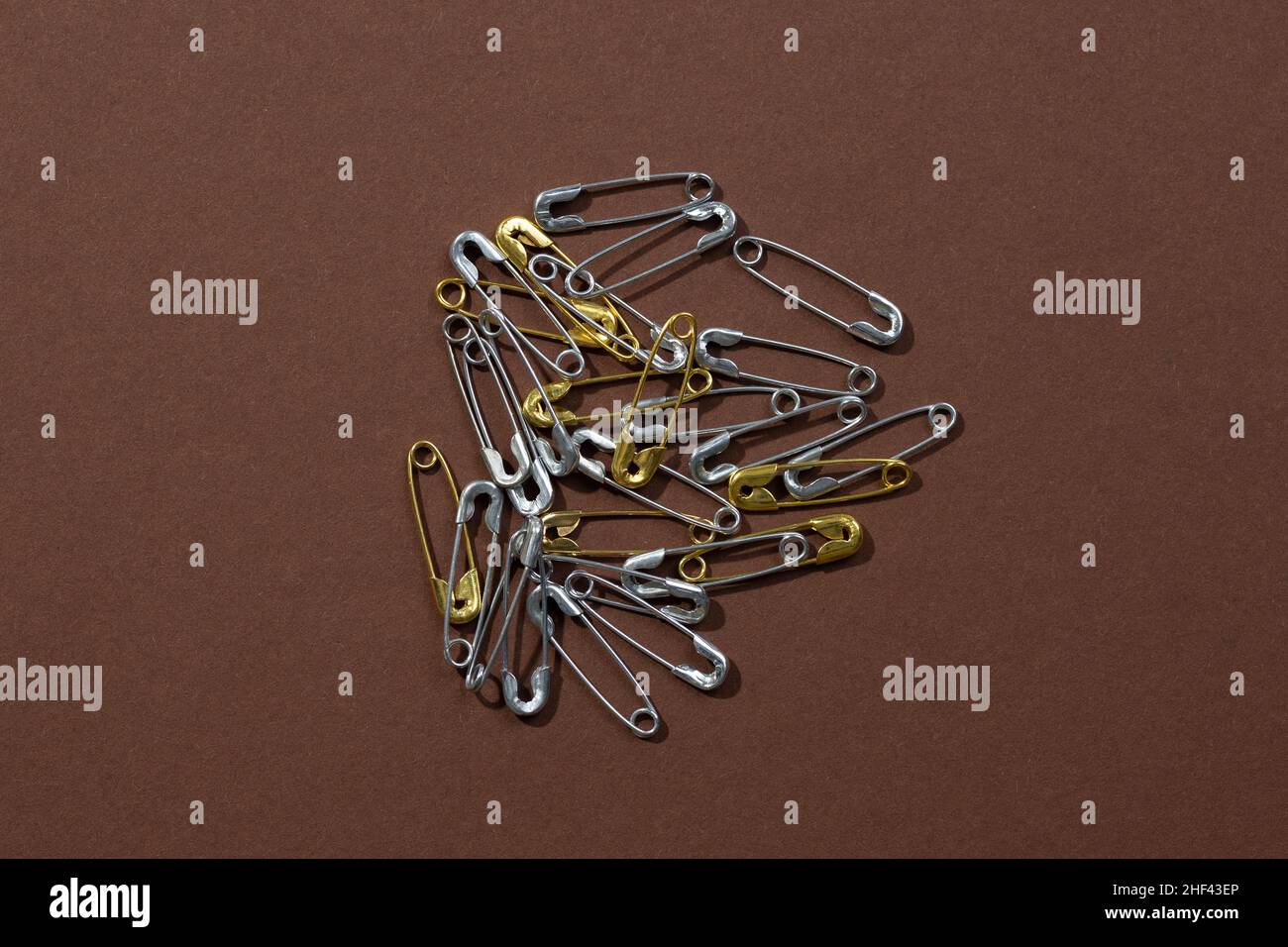 Dark-brown background with tiny silver and gold safety pins scattered chaotically in center. Copy space. Mock up photography. Creative minimalism with Stock Photo