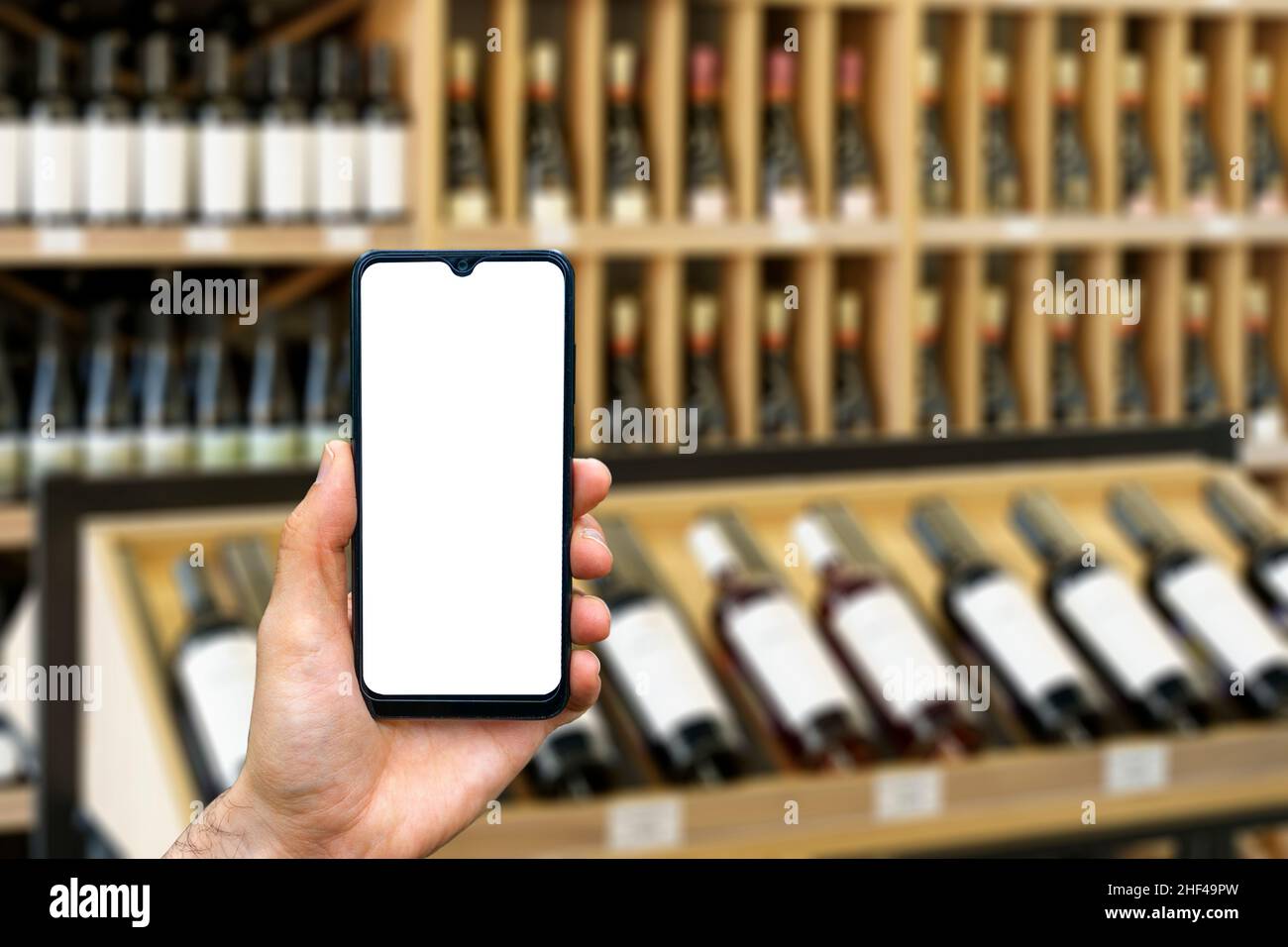 Wine shop with bottles background. Hand with blank smartphone screen