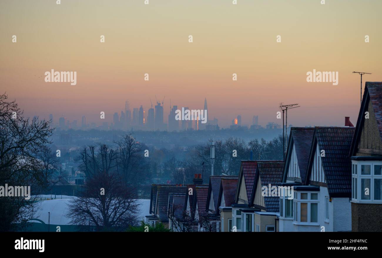 Wimbledon, London, UK. 14 January 2022. Sunrise over central London skyscrapers seen distantly from frosty rooftops of houses in Wimbledon through haze on the day high air pollution level warning is announced. Credit: Malcolm Park/Alamy Live News. Stock Photo