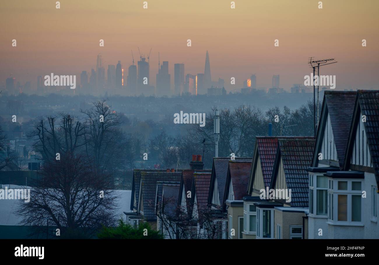 Wimbledon, London, UK. 14 January 2022. Sunrise over central London skyscrapers seen distantly from frosty rooftops of houses in Wimbledon through haze on the day high air pollution level warning is announced. Credit: Malcolm Park/Alamy Live News. Stock Photo