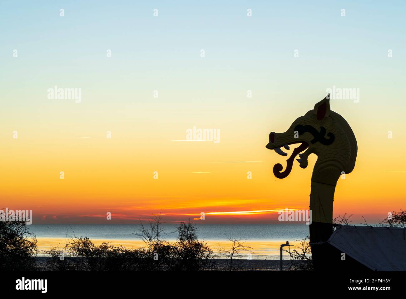 The dawn sky at daybreak over the English Channel  with the silhouette of the figurehead, a dragon's head of the Viking Ship 'Hugin' at Pegwell Bay, Ramsgate, on the Kent coast in England. Stock Photo