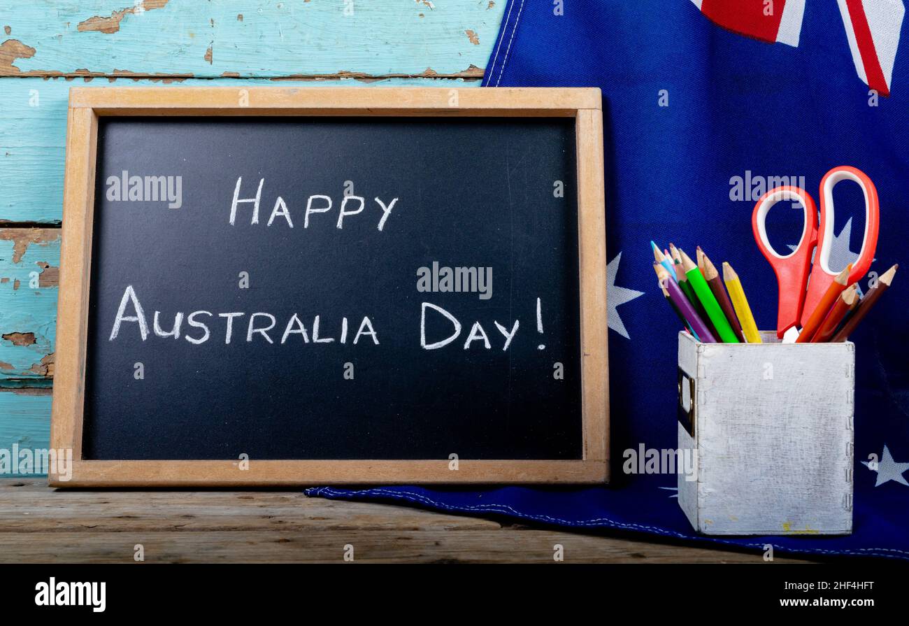 Writing slate with happy australia day text by desk organizer on flag over table Stock Photo